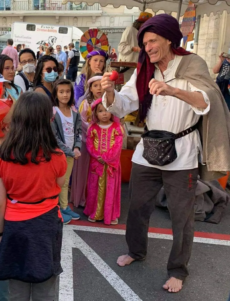 Sylvain, turban pourpre, tend une pomme rouge à des enfants émerveillés lors d'une fête